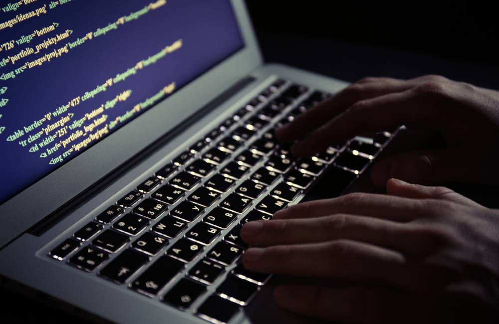 暗い部屋でバックライト付きキーボードを操作し、画面上にシステムのコードが表示されているノートパソコン