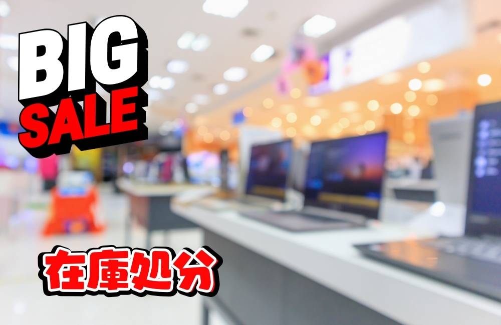 ノートPCの隣に置かれた赤い「SALE」のポップ。決算期やセール期間の大幅な値下げ、掘り出し物を探すイメージ。