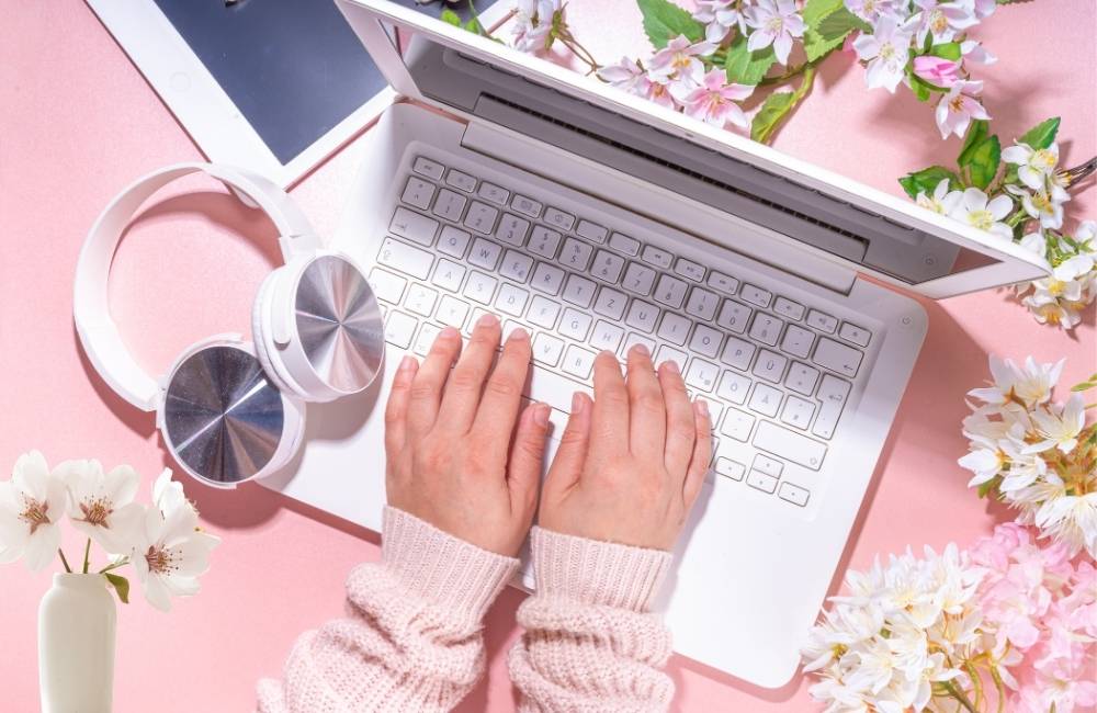 白いノートPCの周囲に桜の造花が飾られ、ピンクの背景で清潔感がある構図。新年度・新生活が始まるシーズンの需要変化を象徴。