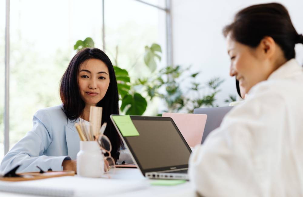 明るいオフィスでノートPCを挟んで向かい合い、真剣に話し合う2人のビジネスパーソン。中古PCの価格や条件について交渉しているイメージ。