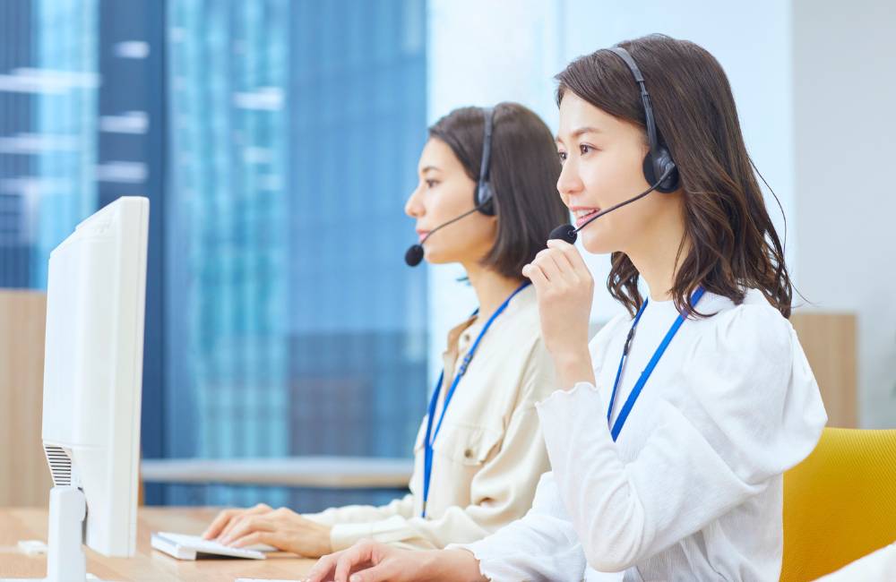 ヘッドセットを装着し、笑顔で電話応対する女性オペレーター（コールセンター）。購入後の手厚いサポート体制を象徴。