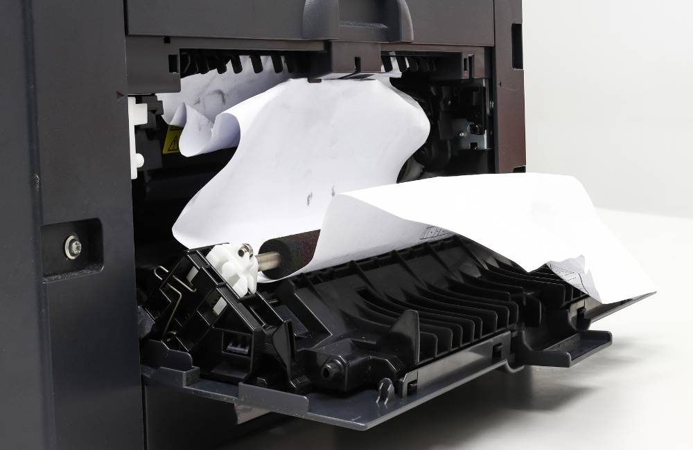 プリンタの内部で紙が詰まっている様子がクローズアップされた画像。紙詰まりの解消など、物理的なトラブルへの対処法を示す。