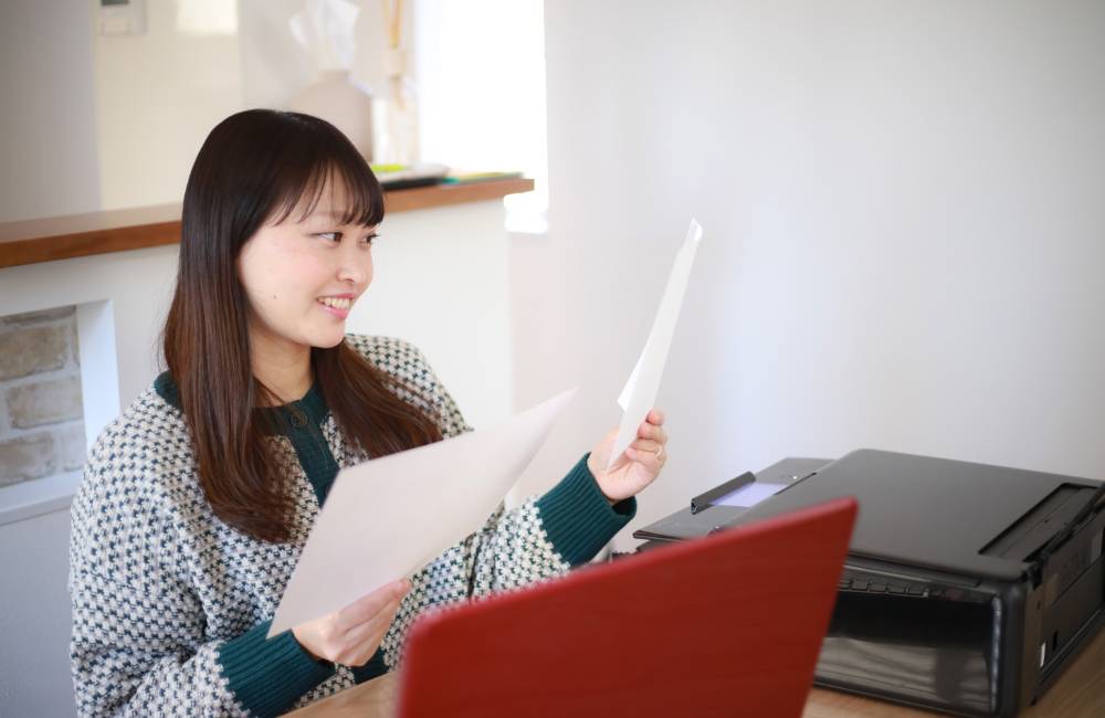 印刷された書類を手に取り、笑顔で確認している女性の画像。問題解決や作業完了後の安堵感を示す「まとめ」のイメージ。