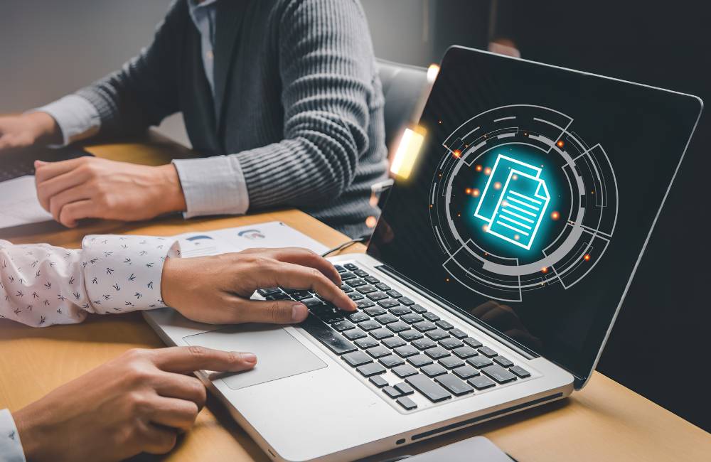 PC画面にデータ保護を示すアイコンが表示され、二人の人物が操作している。中古PCのデータ管理と情報漏洩対策を表現しています。