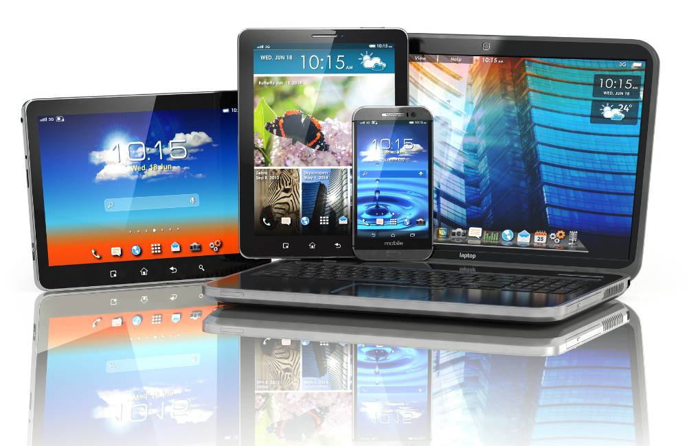 ノートパソコンの上に、タブレット2台とスマートフォン1台が積み重ねて置かれている様子。デジタルデバイスの多様性や世代の違いを象徴。