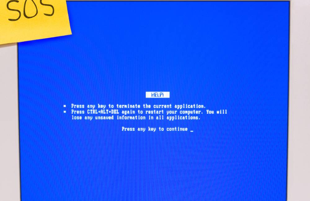 「SOS」の付箋が貼られたパソコンの青いエラー画面（ブルースクリーン）。故障への不安を象徴するイメージ。