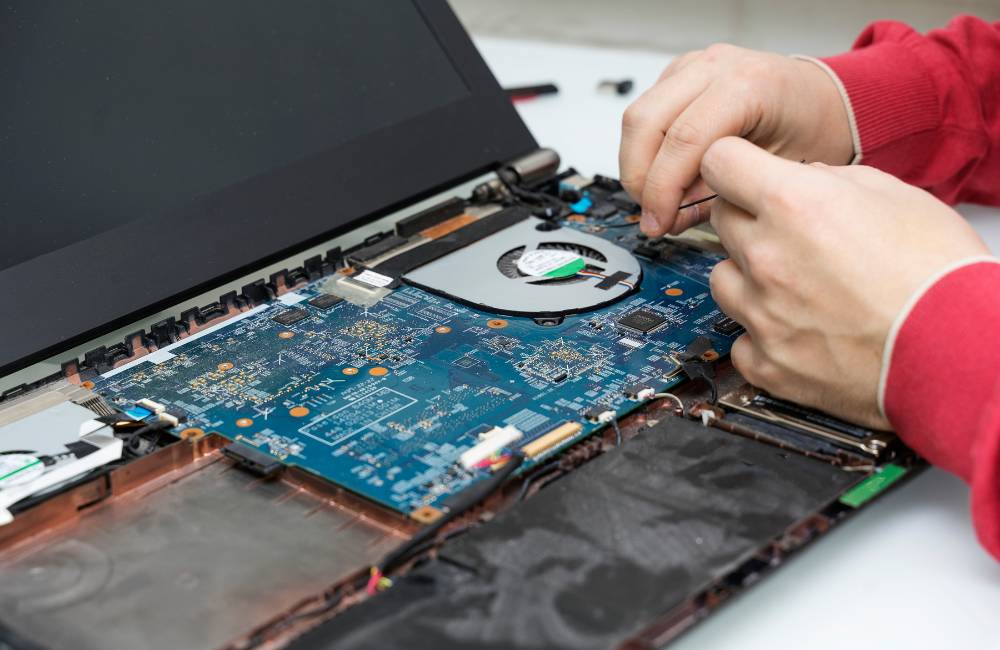 ノートパソコンの裏蓋を開け、精密な内部基板や冷却ファンを指先で慎重に点検・修理している様子。