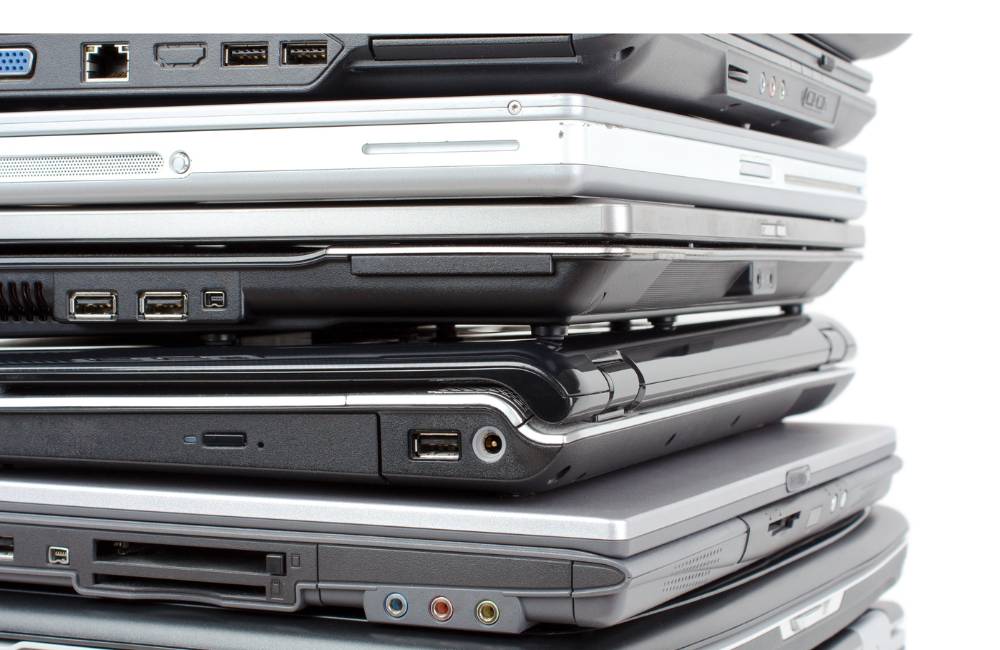 山積みになった大量の古いノートパソコン。安価な部品取りや廃棄リスクを象徴する積み重ねられたPC