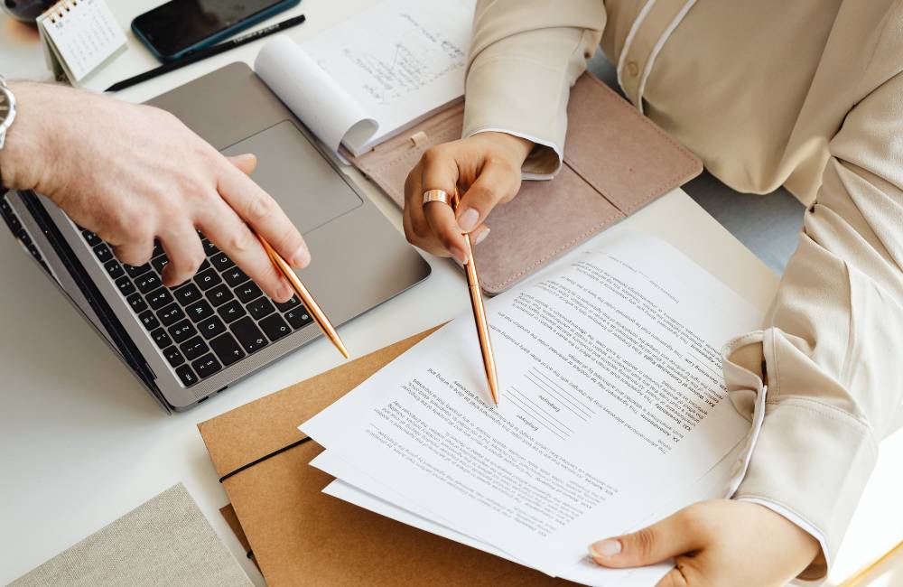 机の上に広げた契約書類の重要な項目を、二人の人物がペンで指し示しながら確認している手元のアップ
