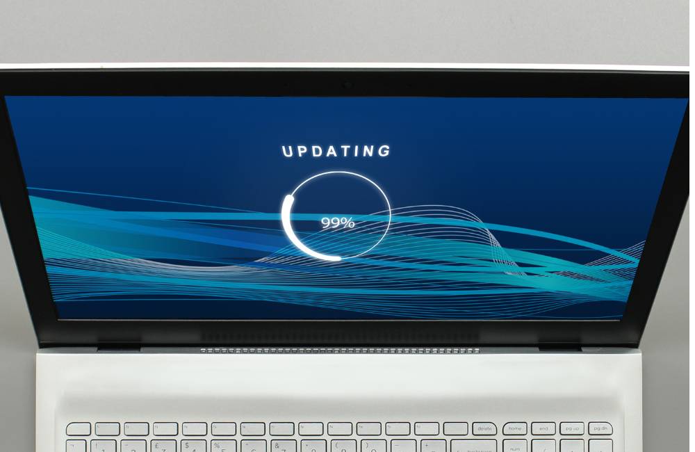 ラップトップパソコンの画面に「UPDATING」と表示され、進捗を示す円形のローディングアイコンが99%を示している。