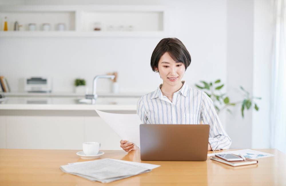 白を基調とした清潔感のあるキッチンカウンターで、笑顔でノートパソコンを操作する女性