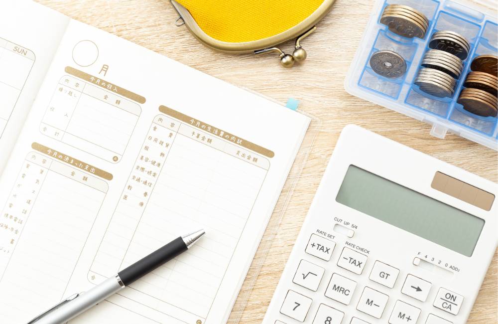 家計簿のようなノートと電卓、小銭入れが並んだデスクの上で、予算を検討しているイメージ