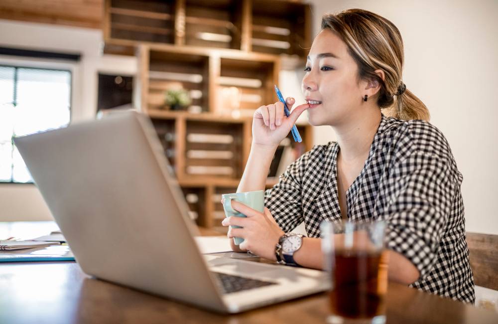 自宅でノートPCを前に座り、考え事をしている男性の背後の写真。在宅ワークやリモート業務に必要な中古パソコンのスペック検討。