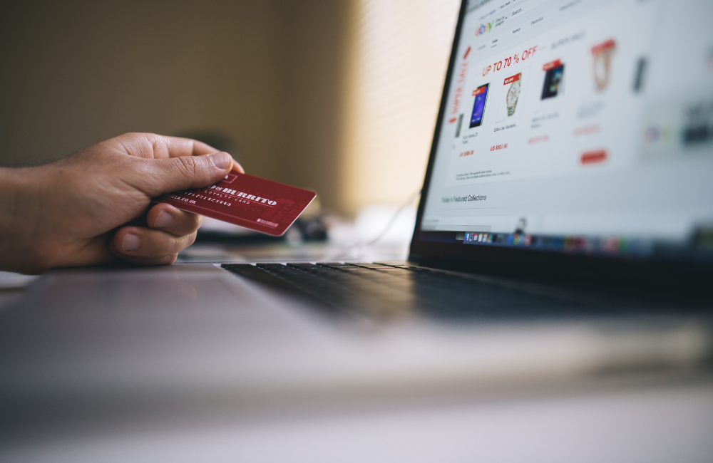 ノートパソコンの前で左手にクレジットカードを持ち、ショッピングサイトの画面を見ている手元