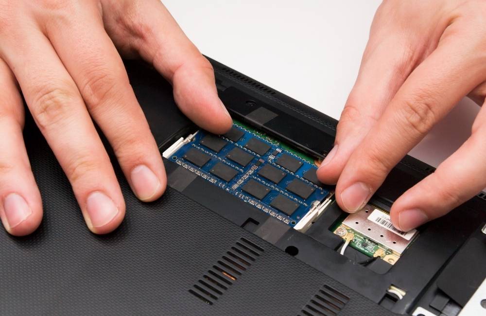 ノートパソコンのメモリスロットに、手作業で新しいメモリ基板を差し込み装着している様子