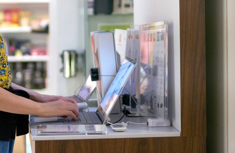 パソコンショップのカウンターで、スタッフがパソコンの画面を見せながら専門的な接客・相談を行っているシーン