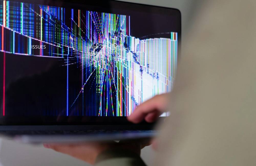 画面が激しく割れ、カラフルなノイズ（縦線）が入ってしまったノートパソコンのディスプレイ。中古品における液晶トラブルや故障リスクへの注意を促すイメージ。