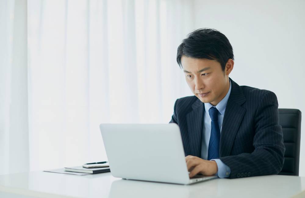 スーツ姿の男性がオフィスでノートパソコンに向かって作業している写真