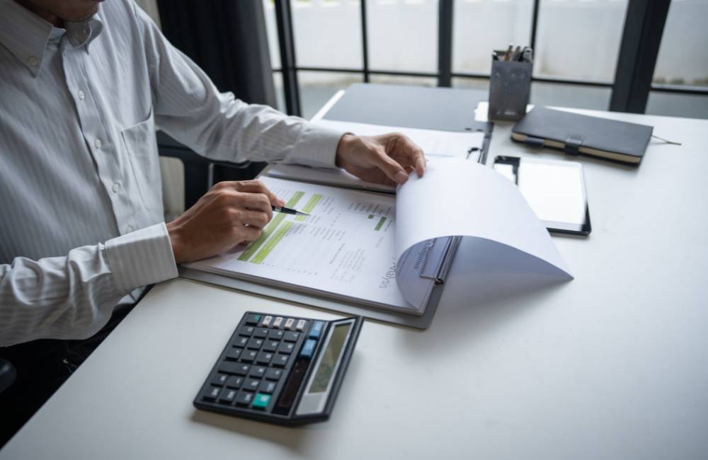デスクで書類をめくり電卓が置かれているビジネスマンの手元