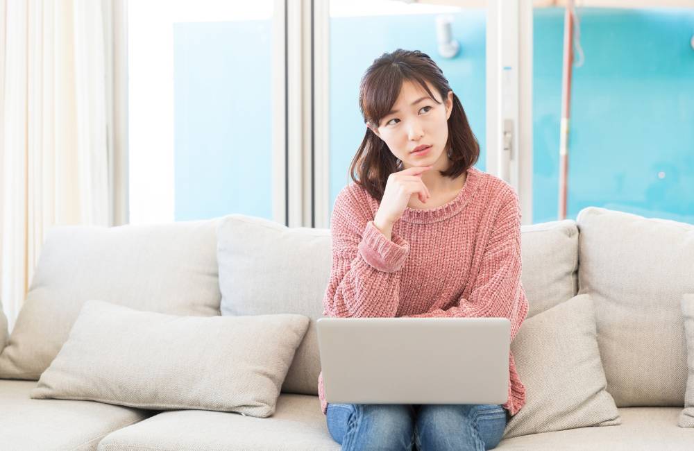 ソファでPCを抱えながら「持ち運びはどうかな?」と考え込む表情が、読者の共感を呼びます。