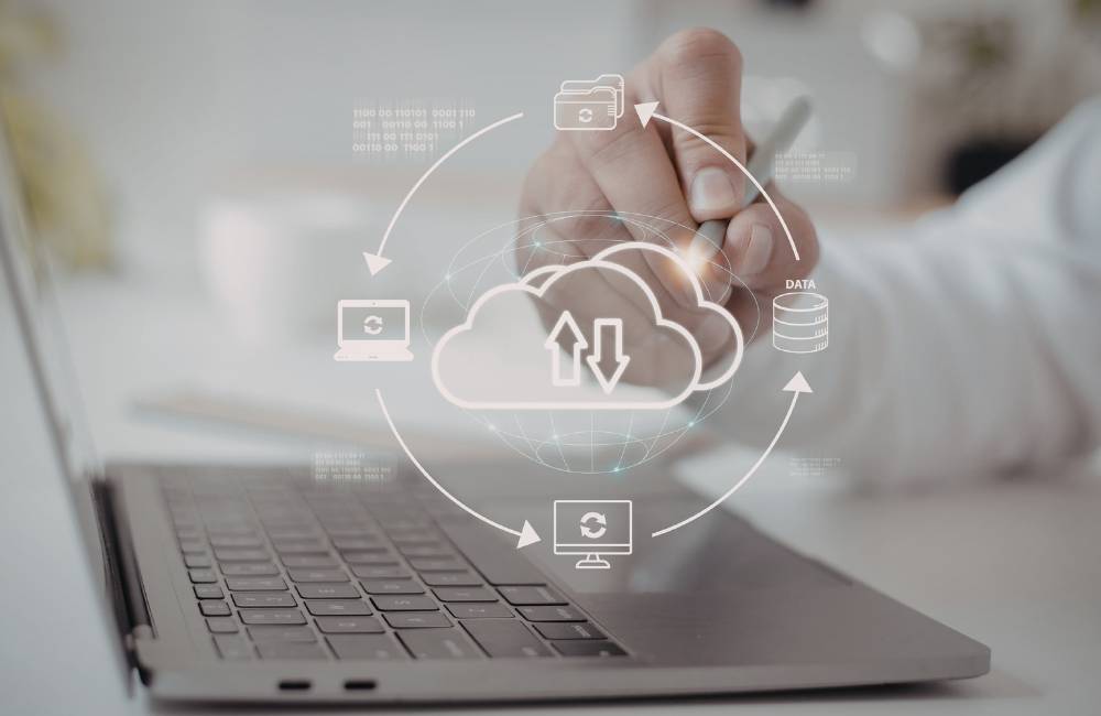 ノートPCの前に、データ共有やバックアップの仕組みを示すアイコンが円を描くように並んでいるイメージ。