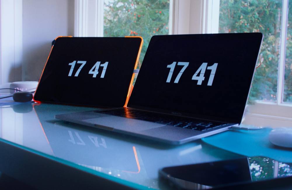 スクに並んだ2つのモニターに、同じデジタル時計の数字が表示されている。正確な動作確認をイメージさせる1枚。