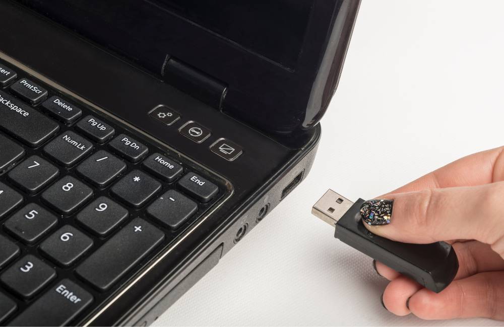 黒いノートPCの側面にあるポートに、銀色のUSBメモリをゆっくりと差し込もうとしている手元のクローズアップ。