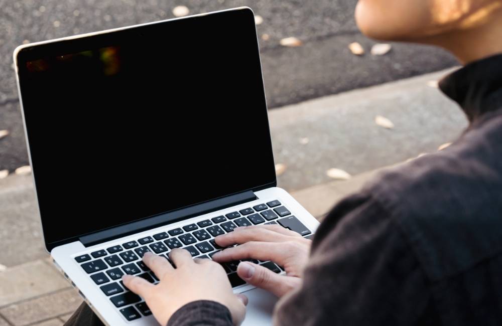 屋外でノートパソコンを前に、どうすればいいか悩んでいる様子の人物