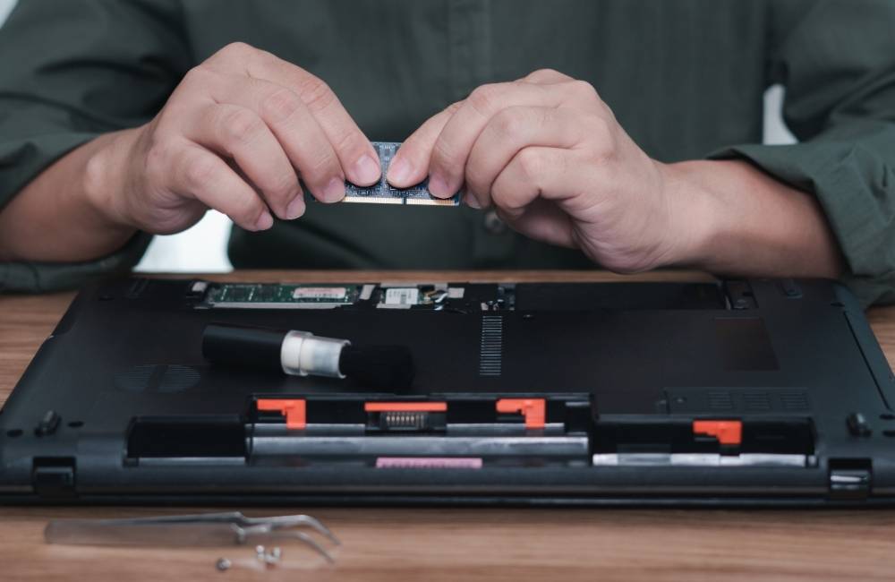 ノートパソコンの裏蓋を開けて、空いているメモリスロットに新しいメモリを両手で装着している場面
