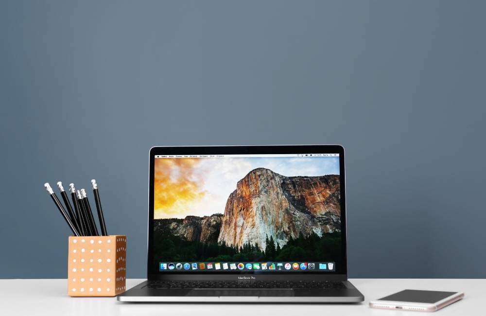 清潔な白いデスクに置かれた、状態の美しいアルミボディのノートパソコン。画面には雄大な山の景色が映し出されている。