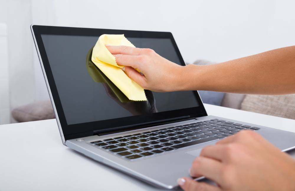 中古ノートパソコンの液晶画面をマイクロファイバークロスで優しく拭き、指紋やホコリを取り除いている様子