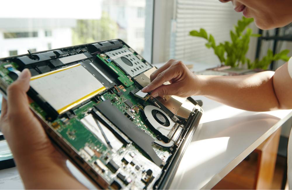 ノートパソコンの内部を開き、緑色の基板や冷却ファンを指で確認している様子。
