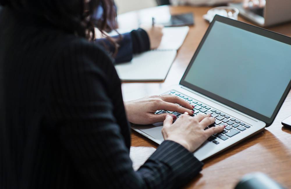 オフィスでノートパソコンに向かい、スムーズにタイピングを行っているビジネスパーソンの後ろ姿。
