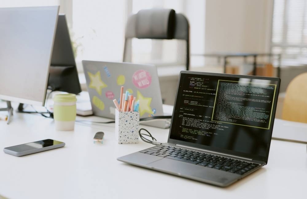 暗い画面に英語のプログラムコードが表示されているノートパソコンが、明るいデスクの上に置かれている様子。