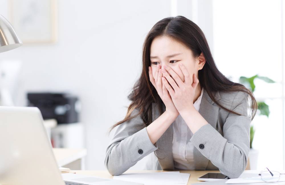 デスクでパソコンの画面を見つめながら、両手で口元を覆って「どうしよう」と不安そうな表情を浮かべている女性の様子。初めての中古PC選びにドキドキしている読者の心境に寄り添う一枚です。