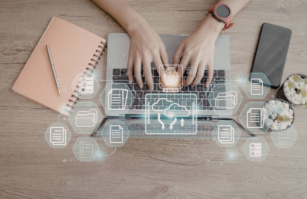 ノートパソコンで作業する手元を真上から見た様子。画面の上には、指紋のマークやデータのフォルダ、クラウドのアイコンがキラキラと浮かび上がり、自分に合った機能を選び出すイメージを表現しています。