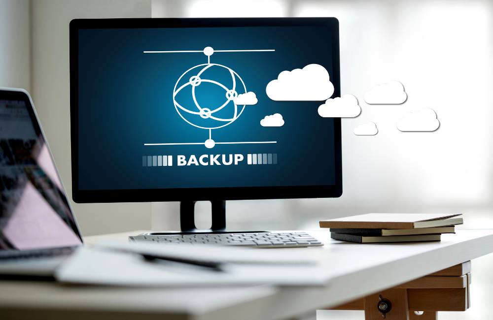 クラウドバックアップを示すアイコンが表示されたパソコン画面と、データを安全に保管するイメージ