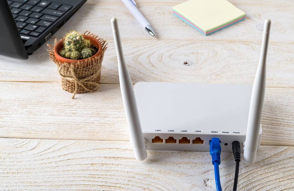 白いルーターの裏側に、青いインターネット用のケーブル（LANケーブル）がしっかりと差し込まれている様子。