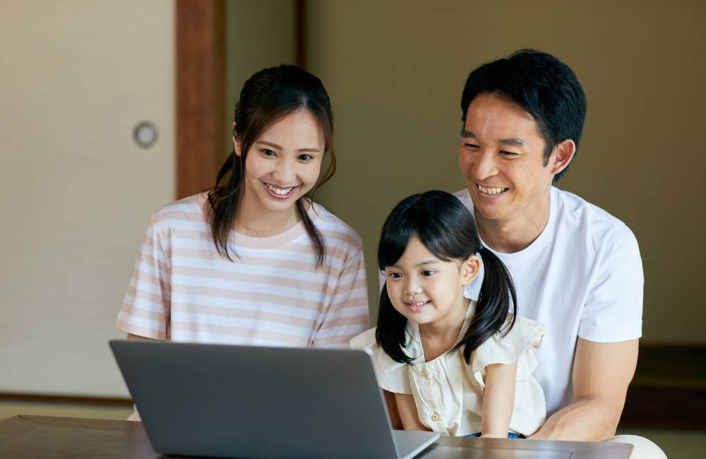 お父さん、お母さん、子供の3人で、1台のPCを笑顔で覗き込んでいる家族の姿。