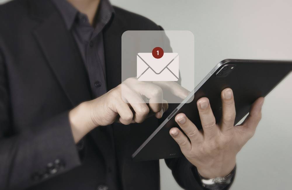 タブレットを操作するビジネスマンの前に、新着通知を示すメールアイコンが浮かび上がっている