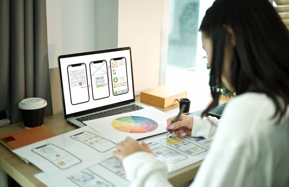 ノートパソコンでCanvaのデザイン画面を確認しながら、チラシやUIデザインを作成している様子