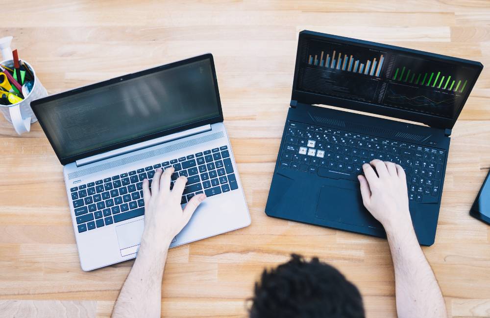 木目のデスクで2台のノートパソコンを使い、コーディングやデータ分析を行っている俯瞰写真