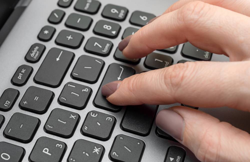 キーボードのキーを指先で深く押し込んでいる手元のアップ写真