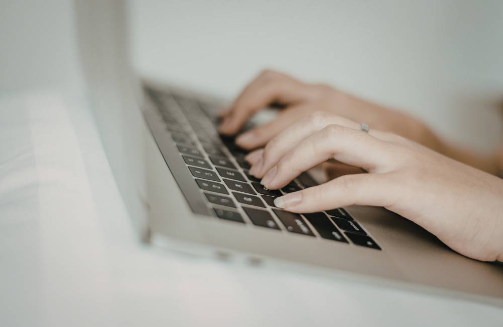 ノートパソコンのキーボードに指を添えてタイピングしている横からのクローズアップ