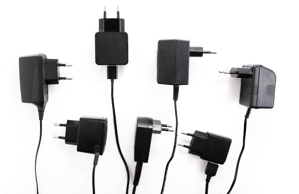 さまざまな種類のノートPC用ACアダプタのプラグや本体が並んでおり、規格を確認する必要があることを示す写真