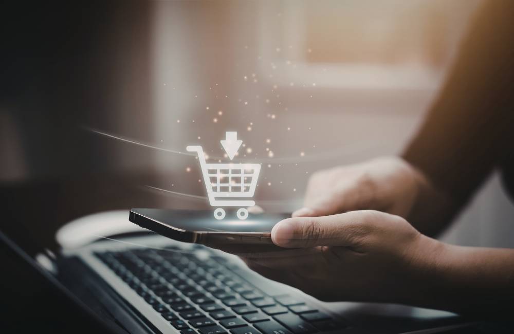 スマートフォン上に浮かぶショッピングカートのアイコン。オンラインショップでのセールやお得な買い物のイメージ。