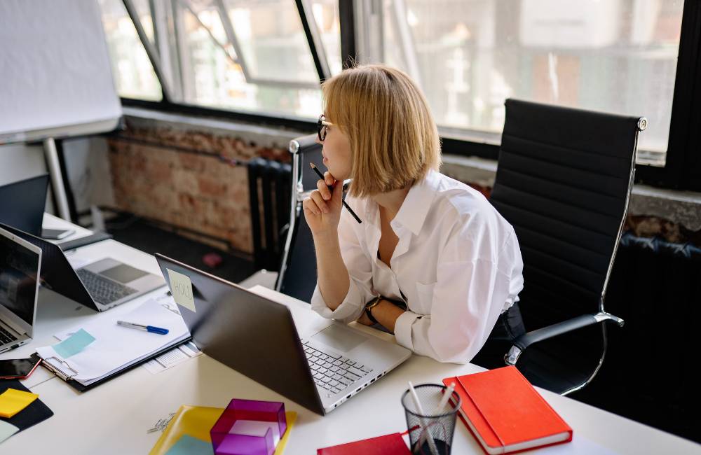 オフィスでノートパソコンを前に考える女性。ビジネスや作業に最適なPCを探しているユーザーのイメージ。