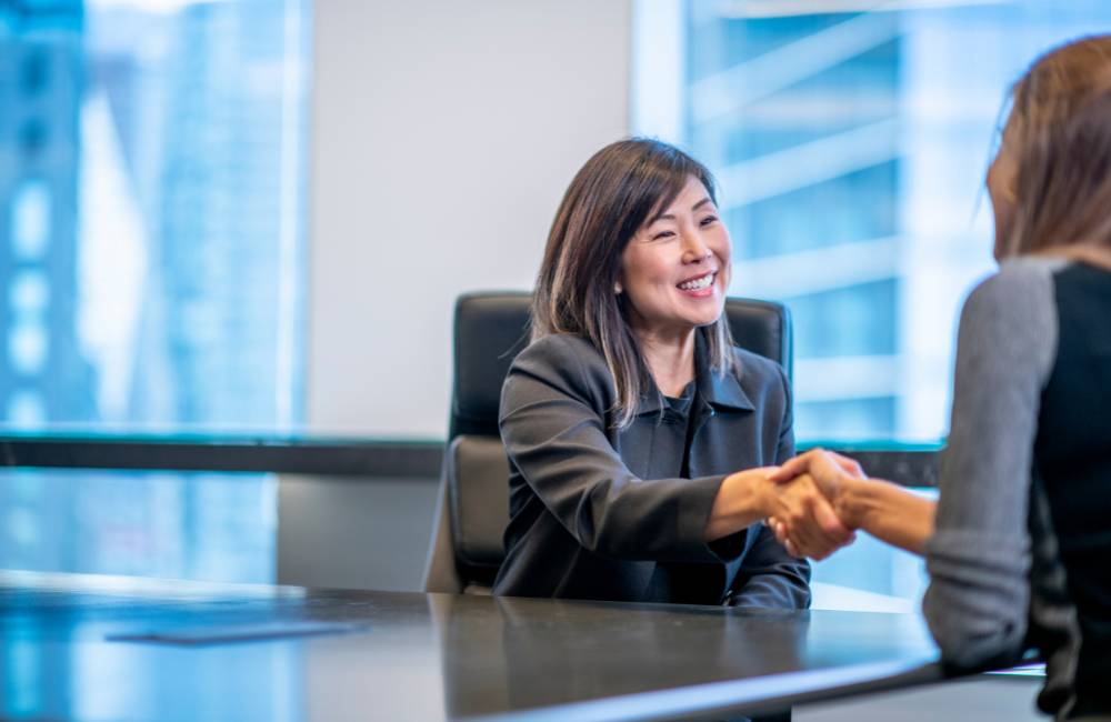 オフィスで笑顔で対面し、握手を交わす女性(ユーザーの満足度と良好な評判をイメージ)
