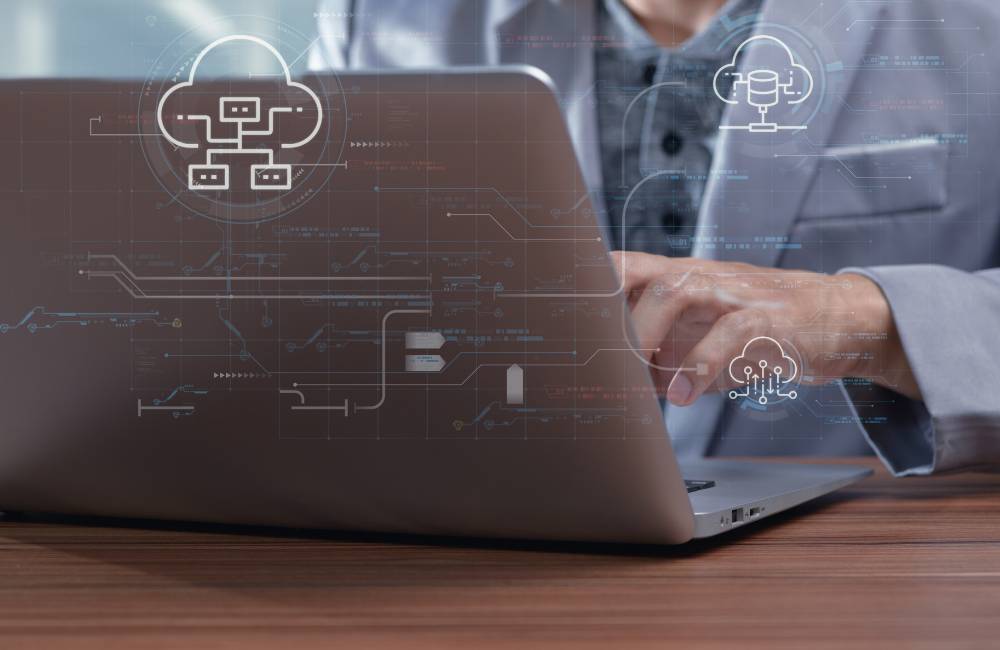 クラウドやネットワークのアイコンが浮かび上がるノートパソコンを操作する様子(高度な技術力と専門性を表現)