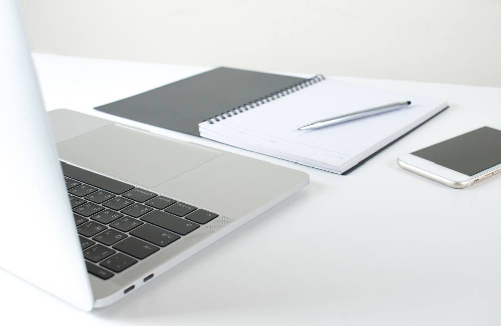 白いデスクの上に、ノートパソコン、開かれたノートとペン、スマートフォンが綺麗に整頓して置かれている様子。全ての情報が整理され、納得のいく購入準備が整った状態を表現。